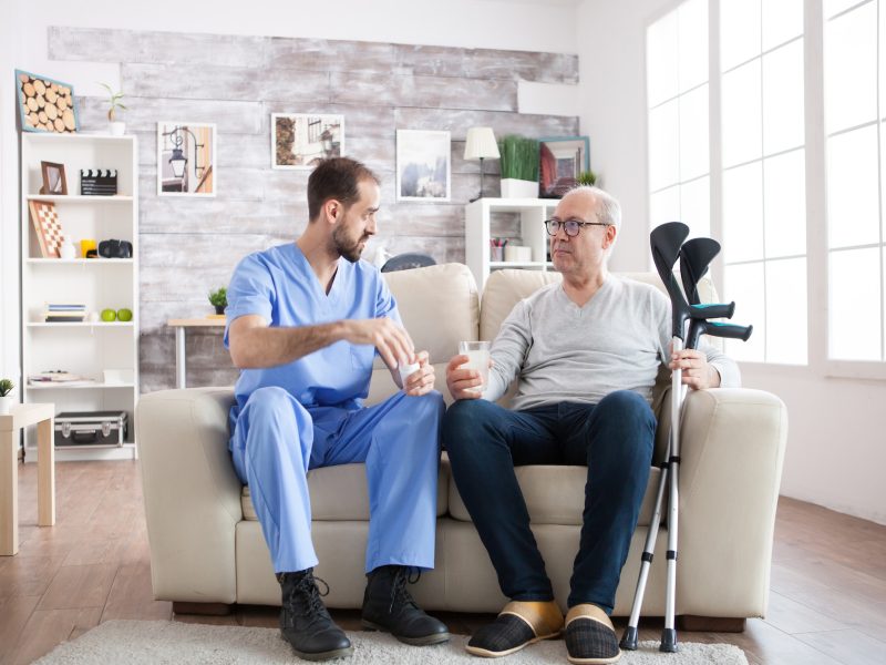 young-male-nurse-in-nursing-home-with-pills-for-senior-man